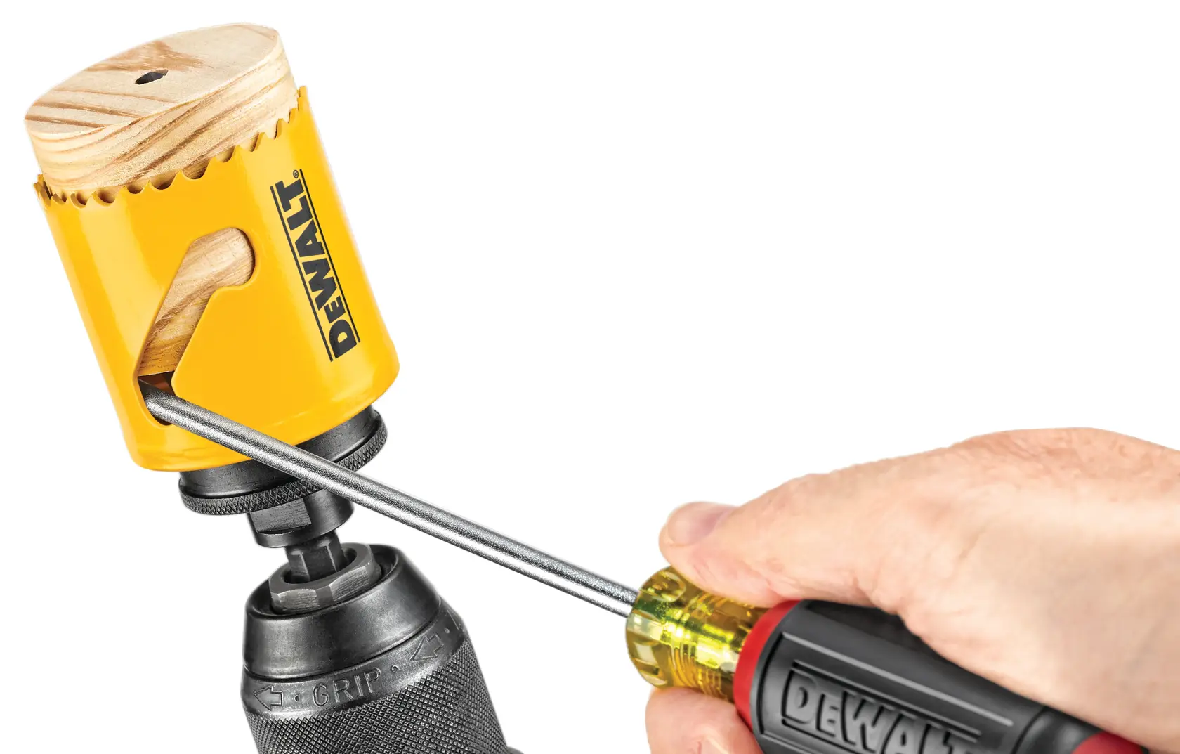 A close-up of a hand using a screwdriver to remove a piece of wood from a yellow DEWALT hole saw attached to a drill.