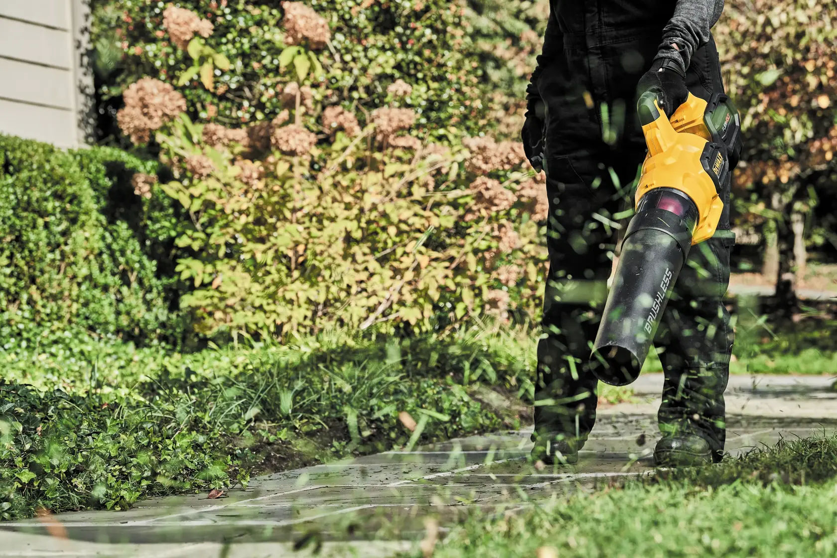 FLEXVOLT Brushless Cordless Handheld Axial Blower being used to blow grass blades off a passageway