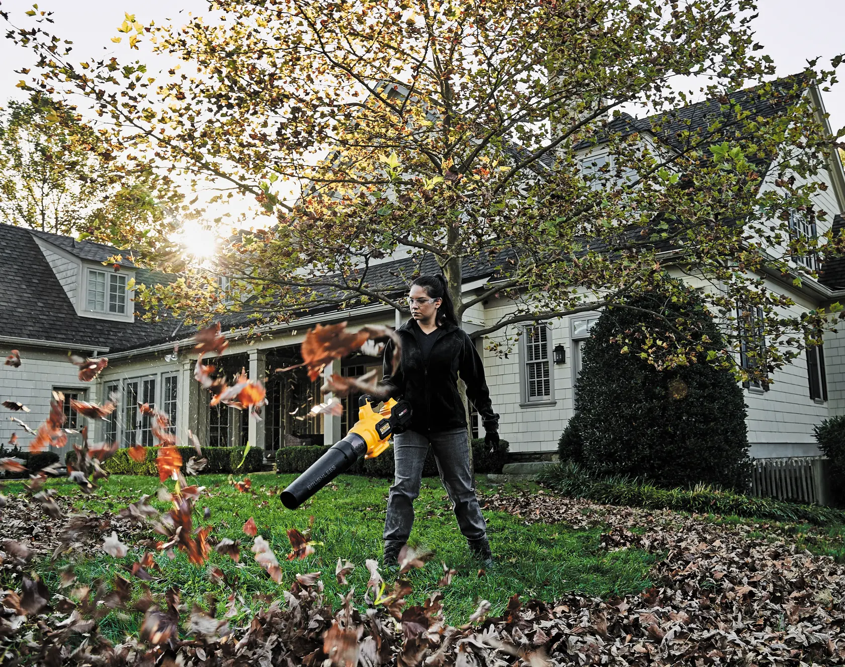 FLEXVOLT Brushless Cordless Handheld Axial Blower being used by a person to clear leaves off ground in a lawn