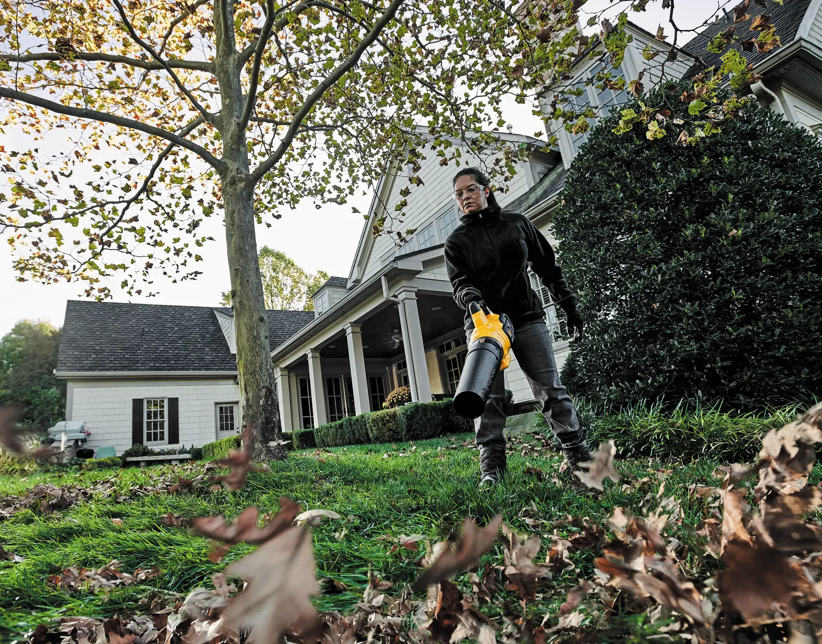 FLEXVOLT Brushless Cordless Handheld Axial Blower being used by a person to clear leaves off ground in a lawn