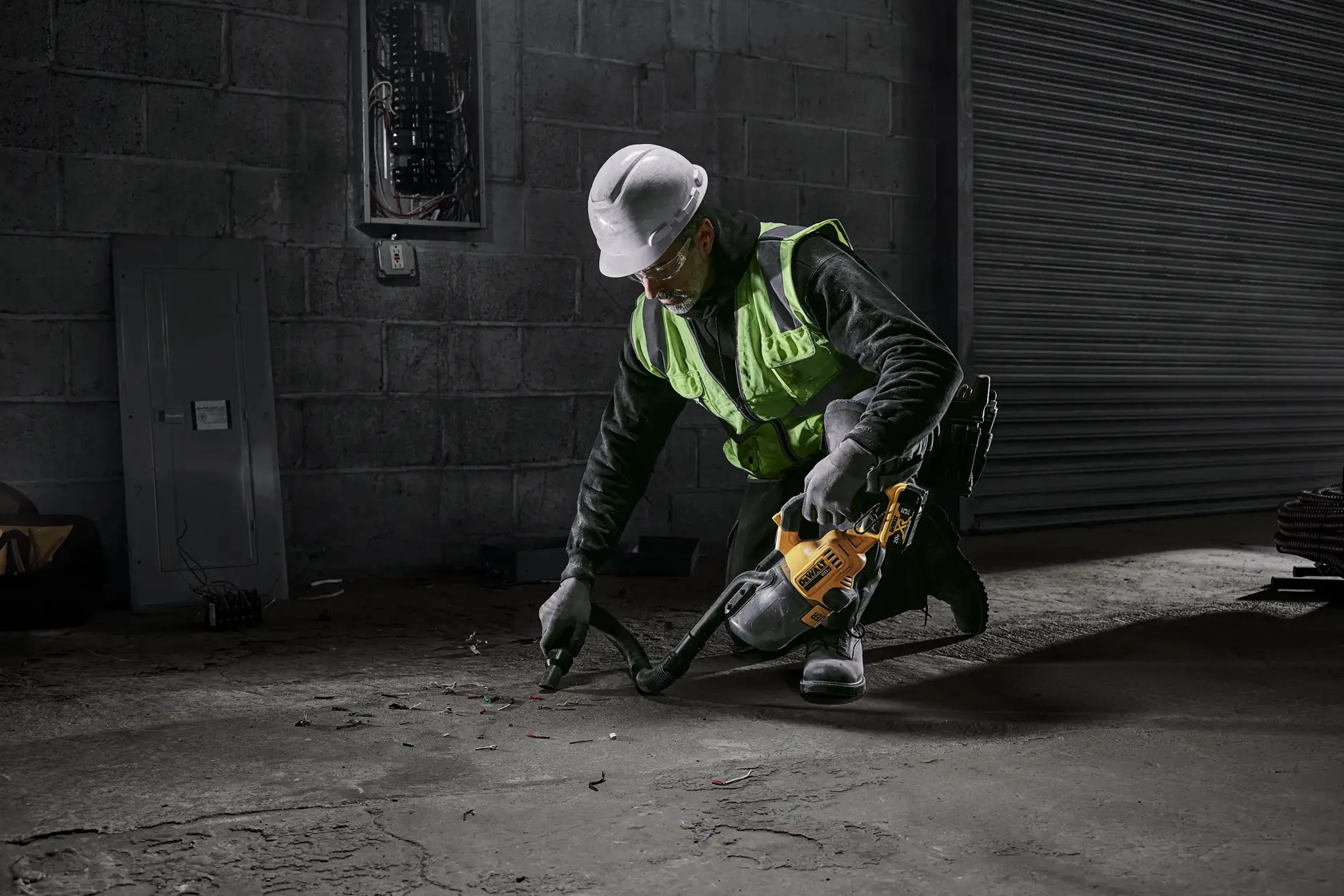 Male electrician using DEWALT 20 MAX* Hand Vacuum with flexible tube and crevice nozzle accessories vacuuming up small screws, nuts, dried caulk, electrical wire insulation, and electrical wire cuttings. DEWALT 5AH battery is being used.