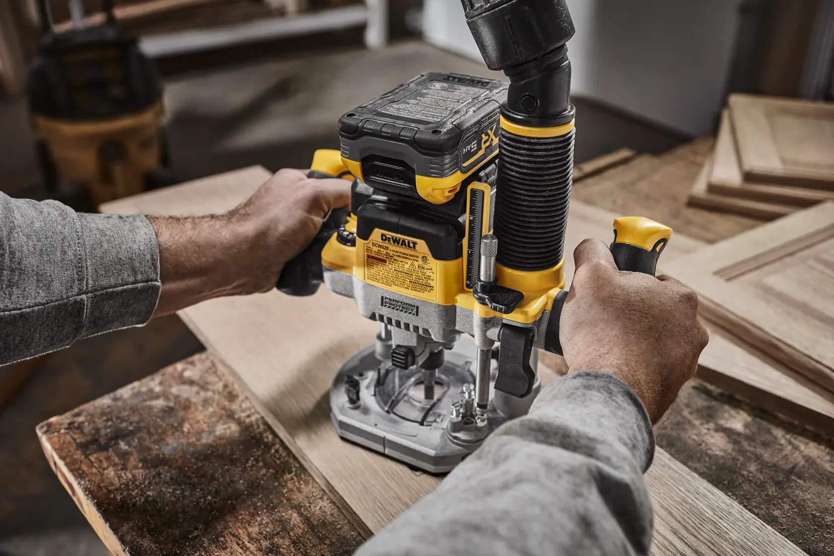 DEWALT XR 20V MAX* Plunge router with 20V MAX* XR 5 ah battery on wood surface in use dust shroud being used. Backside view of tool