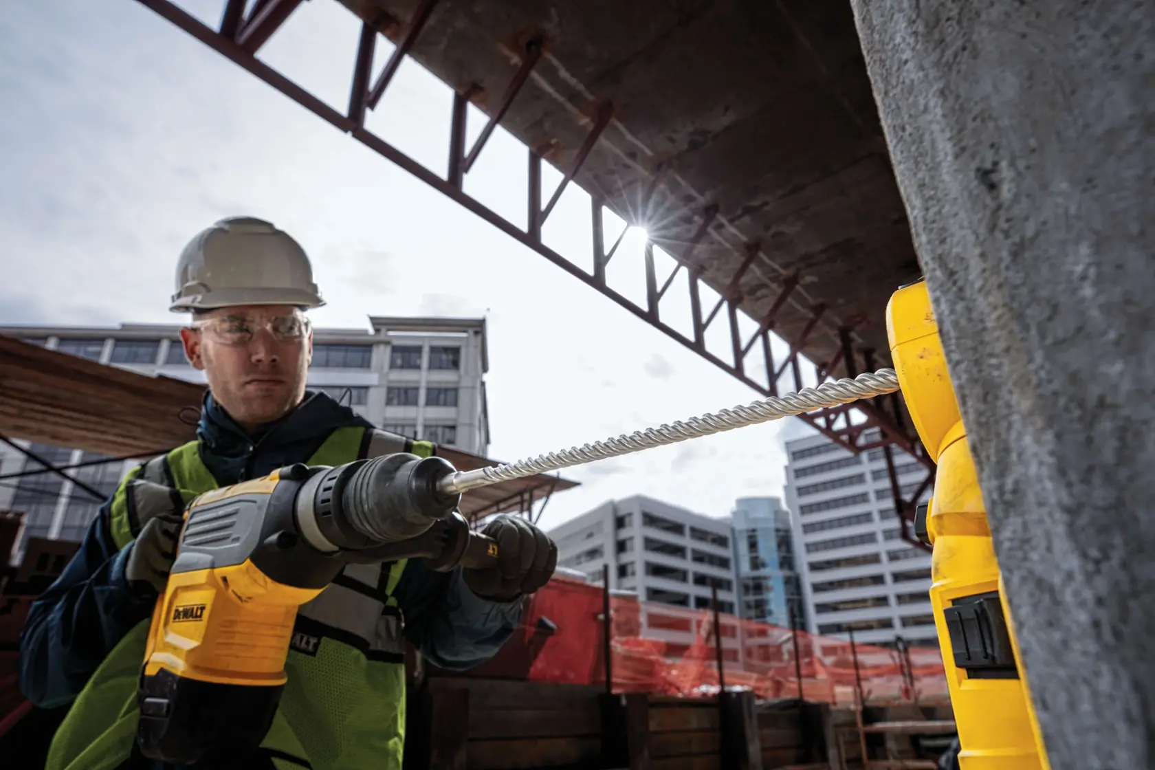 SDS Max High Impact Carbide 4 Cutter Drill Bit being used by worker to drill through concrete wall at outdoor work site.