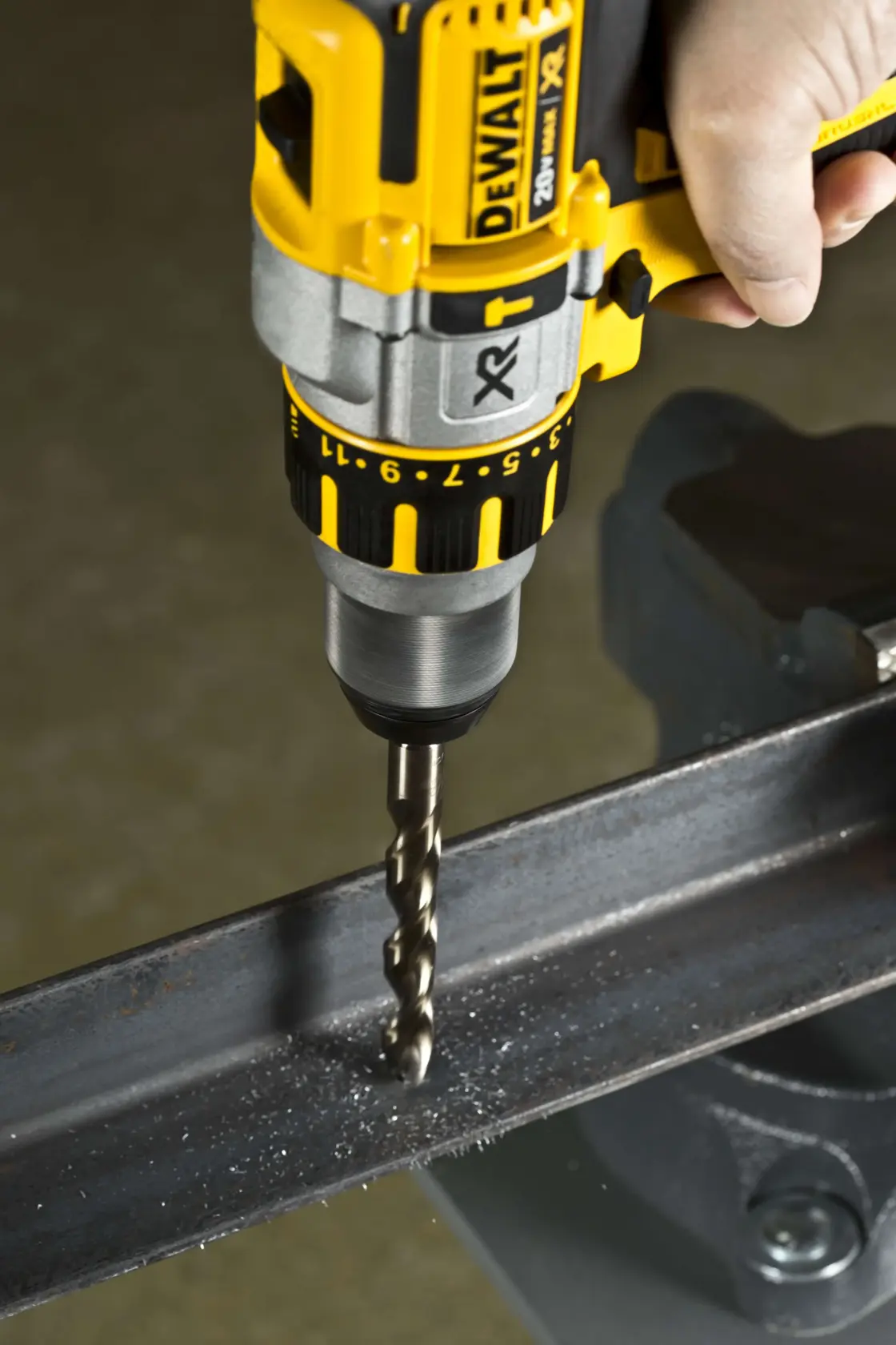 A close-up of a DEWALT power drill being used to drill into a metal beam, with metal shavings visible around the drill bit.