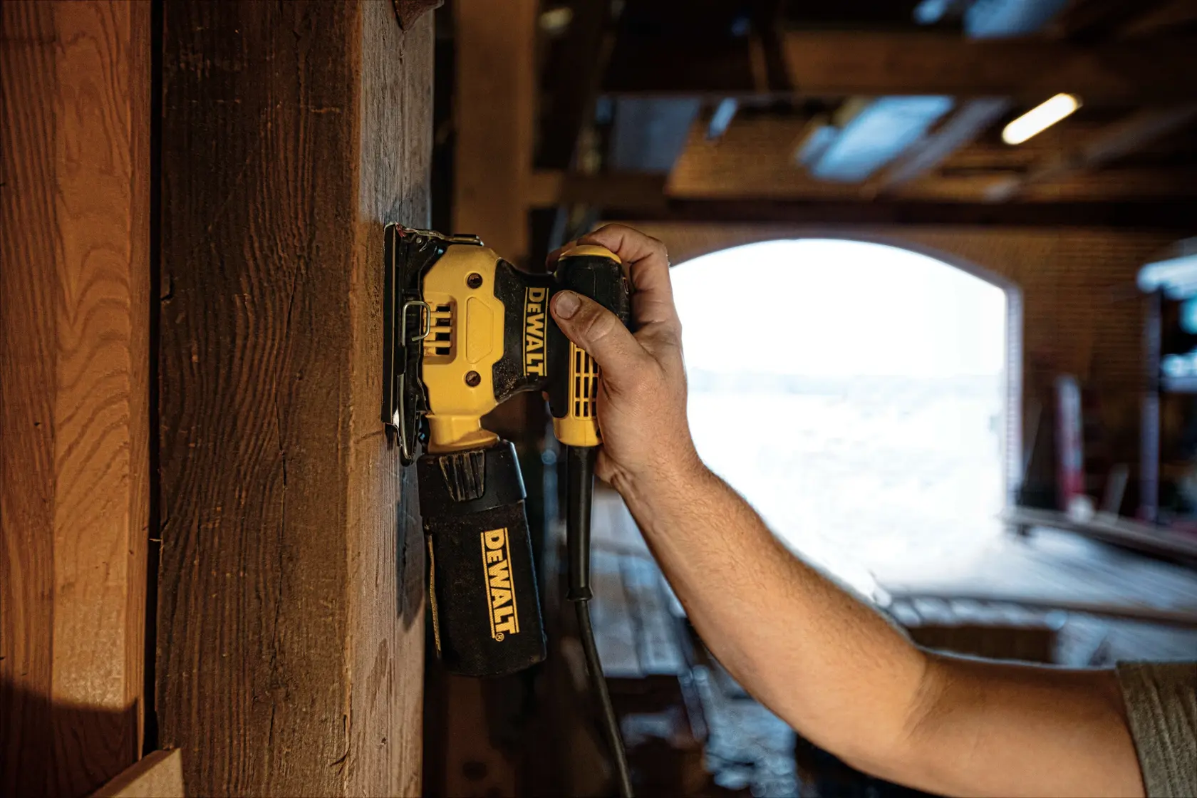 One quarter inch sheet palm grip sander sanding on a wooden wall at a worksite.