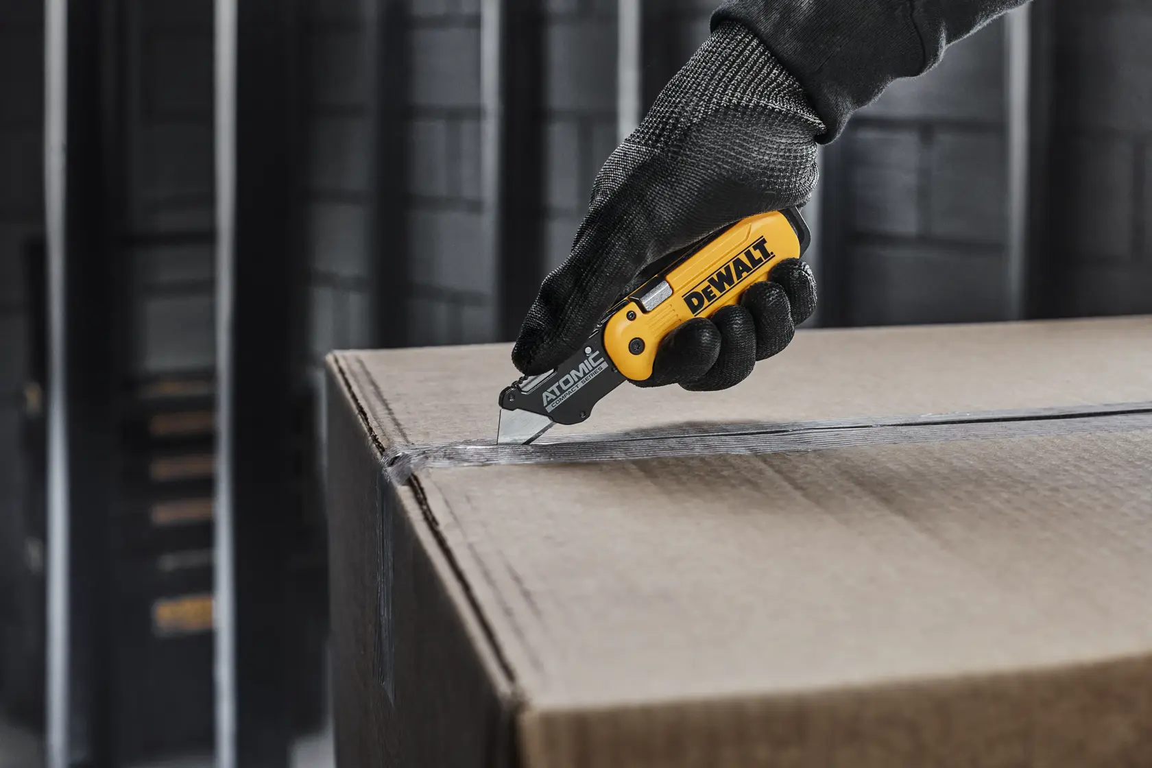 DEWALT ATOMIC knife with user cutting open a cardboard box