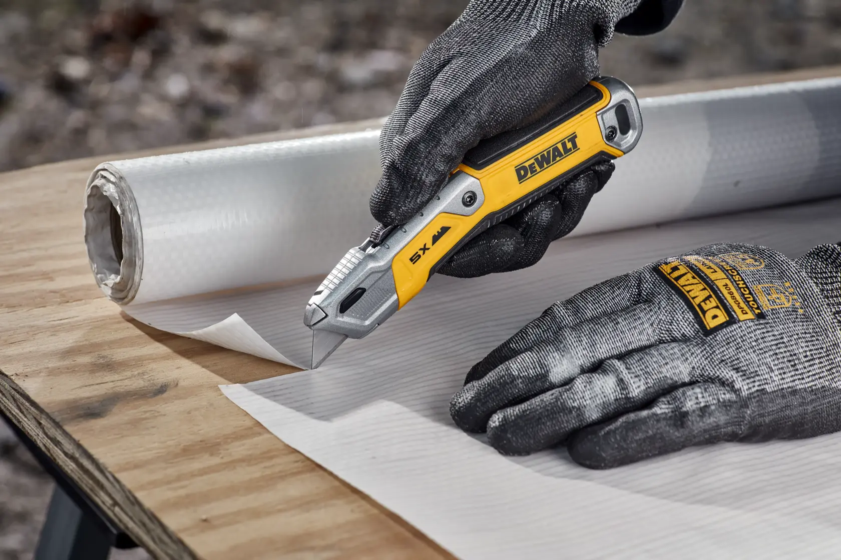 Worker cutting house wrap on plywood surface with DEWALT® DWHT10998 Utility Knife