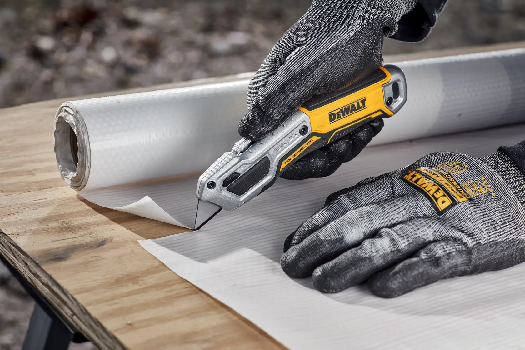 Worker cutting house wrap on plywood surface with DEWALT® TOUGHSERIES™ DWHT10999 Utility Knife
