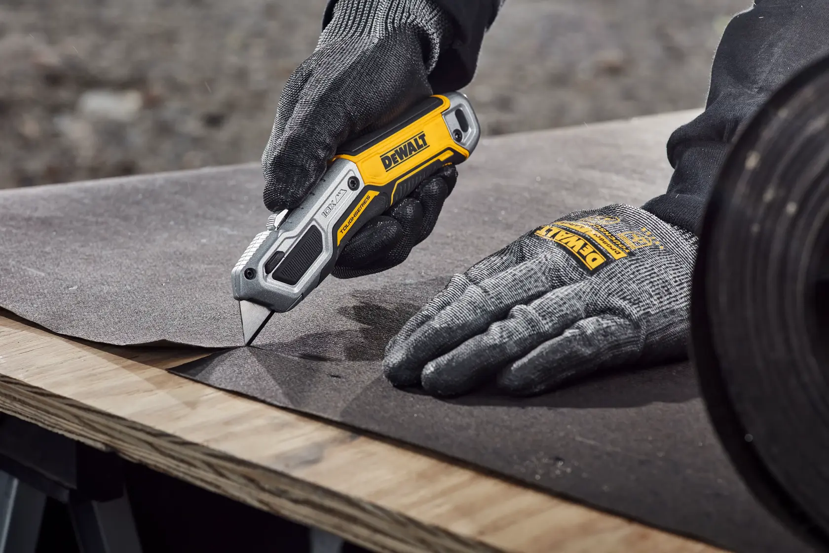Worker cutting tar paper on plywood surface with DEWALT® TOUGHSERIES™ DWHT10999 Utility Knife