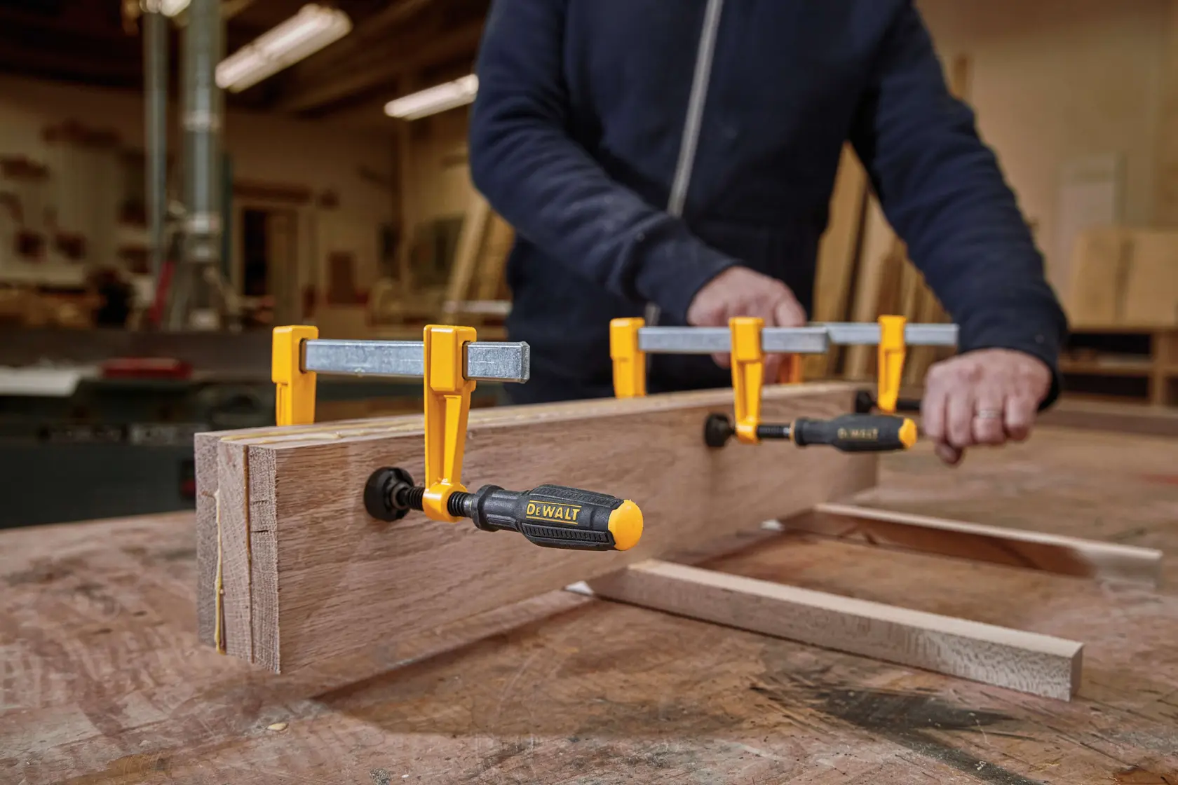 Close up of  4 inch Bar Clamps being used on wooden structures by a person in a workshop.
