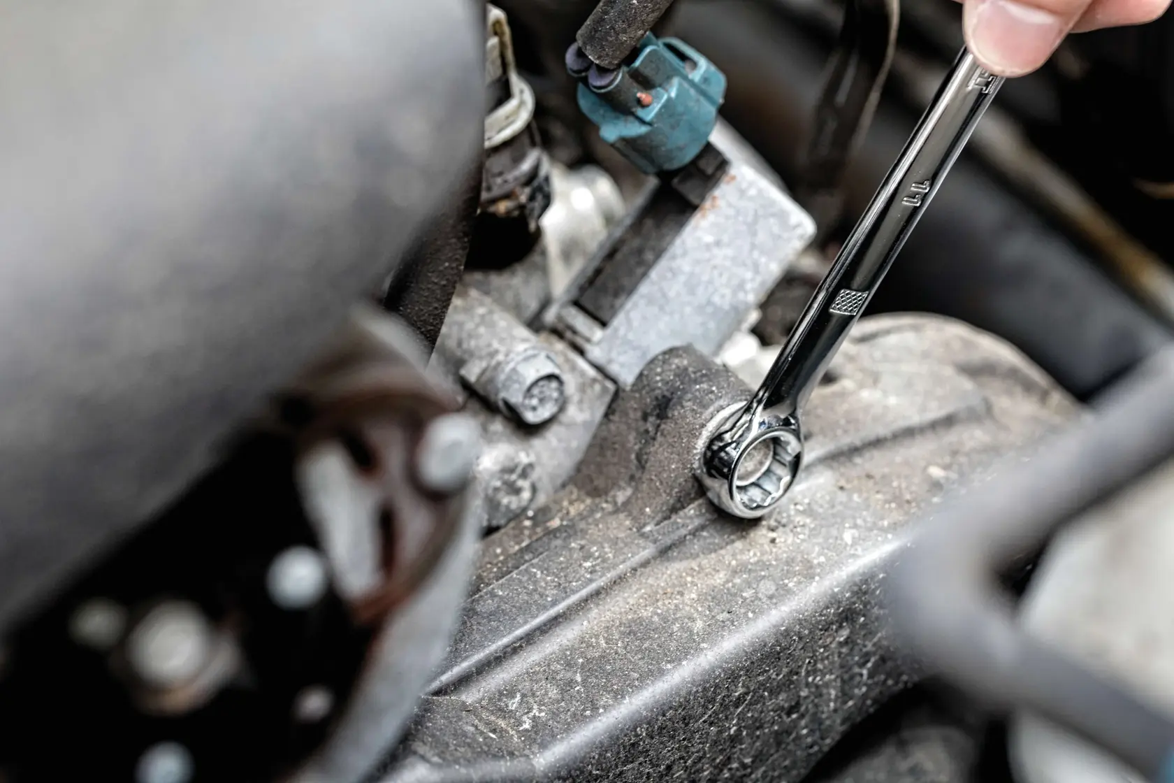 A close-up of a hand using a DEWALT ratcheting wrench on a bolt in an engine compartment.