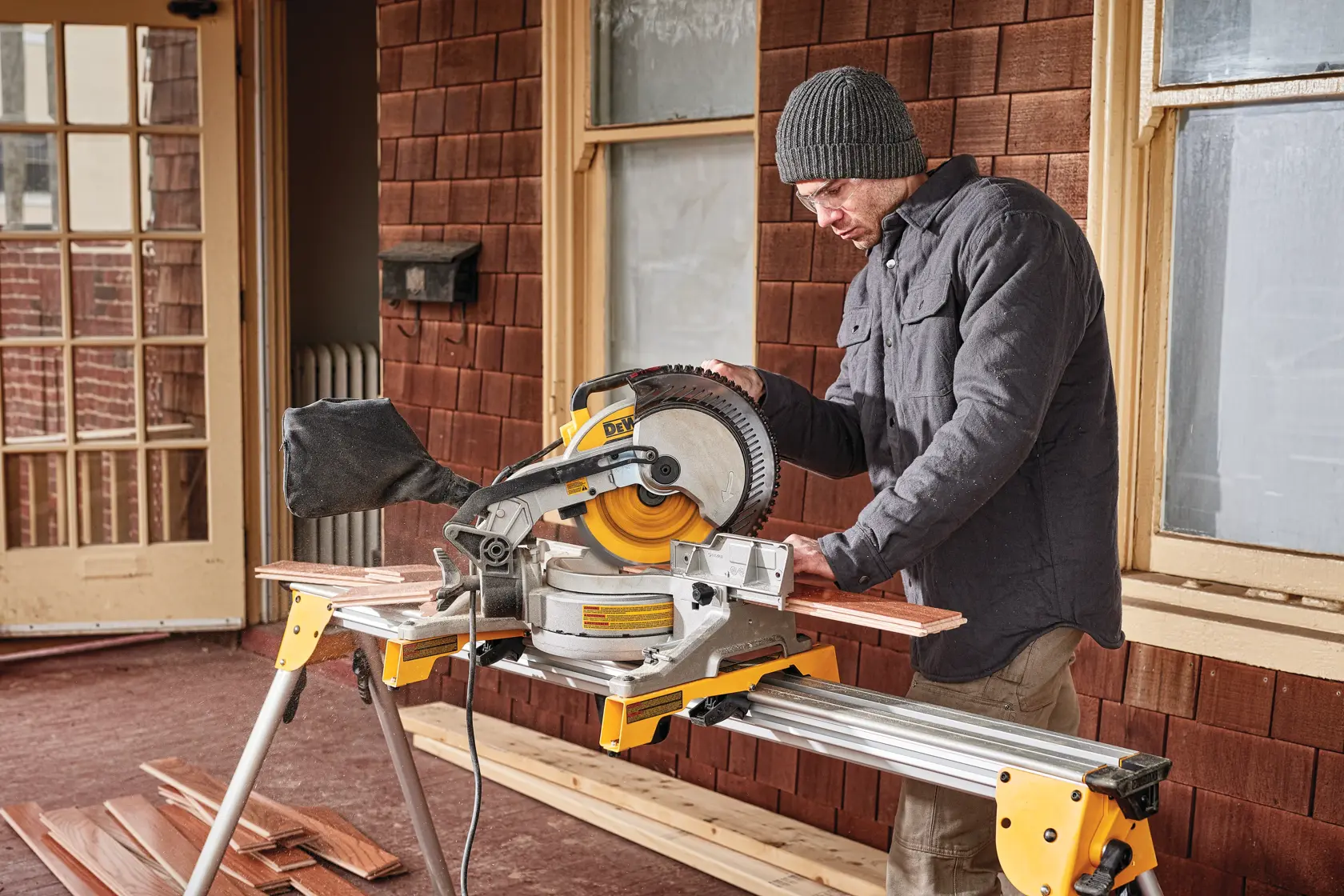 Electric single bevel compound miter saw being used by a person to cut wood.