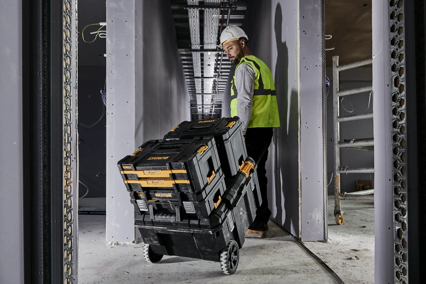 Construction worker pulling a mobile TSTAK job chest along a corridor on a construction site. The chest has x3 Tstak cases connected on top of it